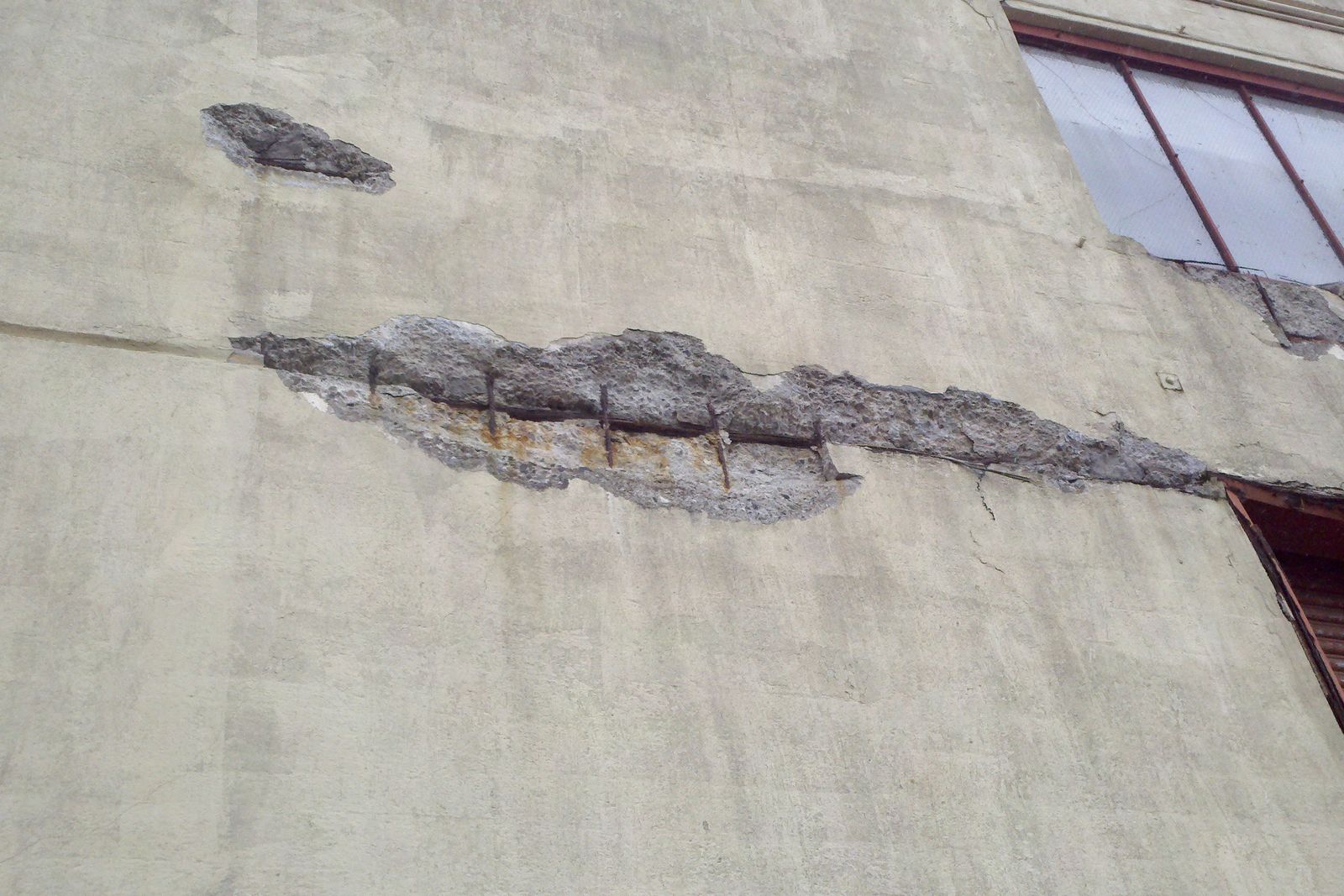 Desplacamento do concreto em parede de edificação à beira-mar, com barras de armadura corroídas expostas ao longo da fissura