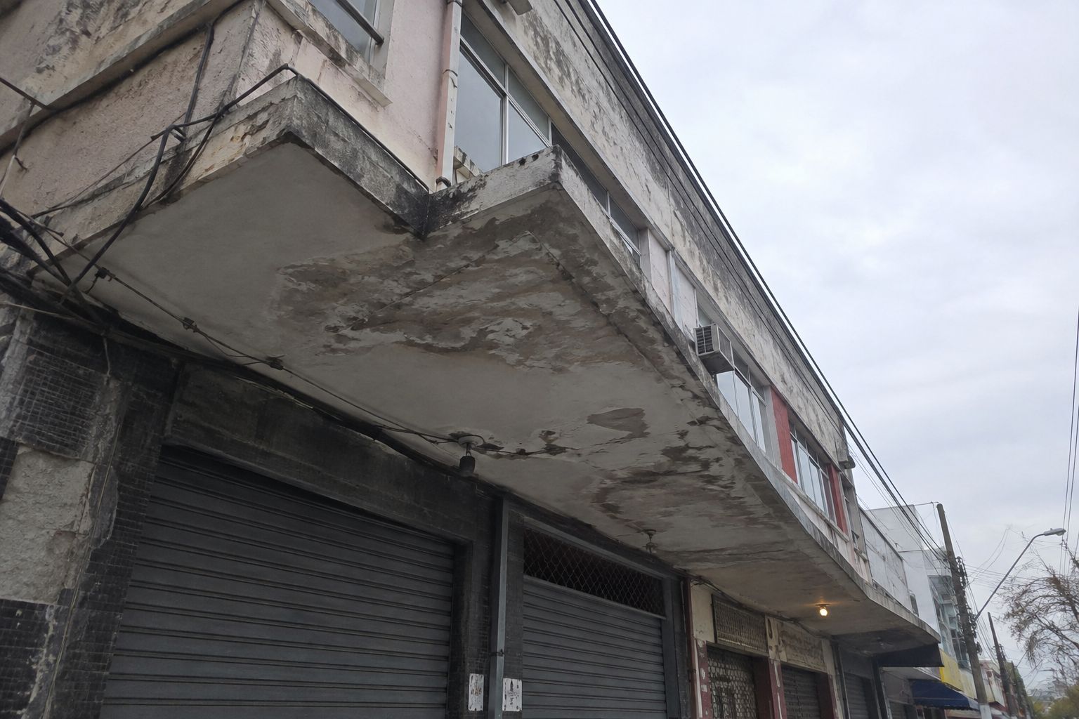 Marquise de concreto em balanço sobre a calçada, vista de baixo, com manchas de umidade na face inferior